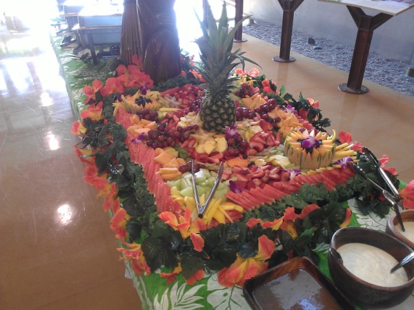 Large diamond-shaped fruit and vegetable carving platter with a whole pineapple centerpiece, set up under a park pavilion