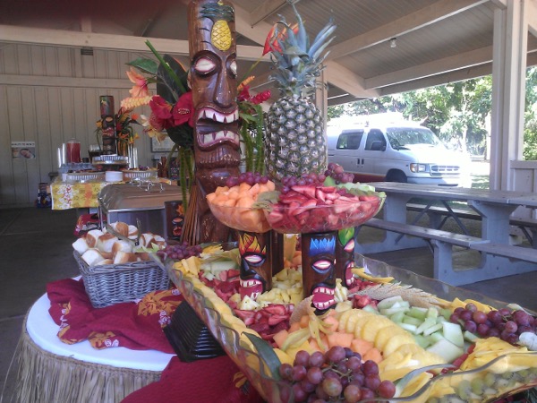 Fruit display carved into a boat shape with carved tiki totems and a whole pineapple centerpiece