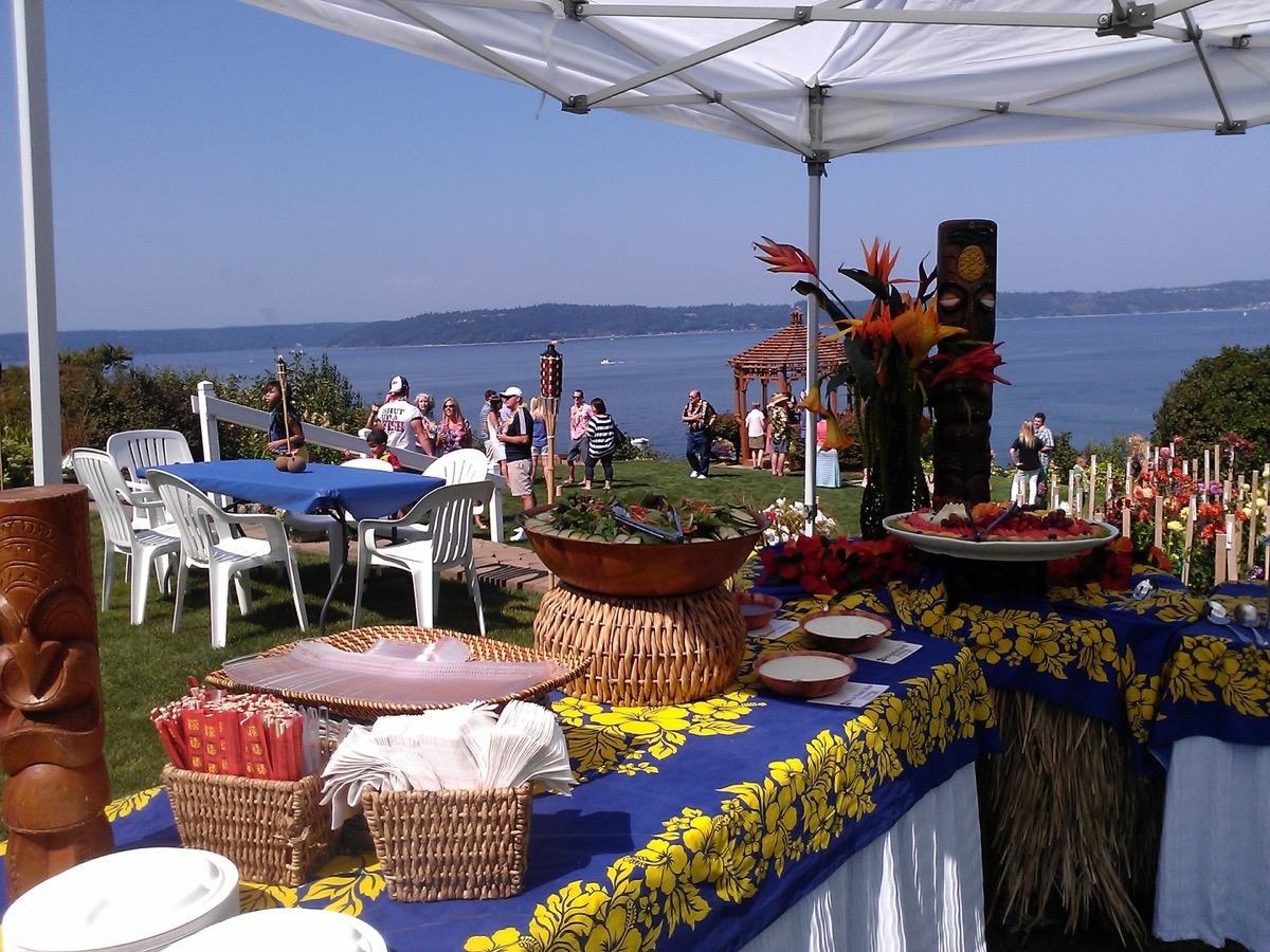 Guests mingling near tiki torches at a waterfront reception under a catering tent